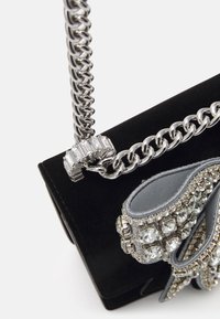 Czarna aksamitna torebka na ramię z srebrnym łańcuszkiem, ozdobiona teksturowaną szaro-białą kokardą i dużymi cyrkoniami. Stabilna podstawa, kompaktowy kształt.