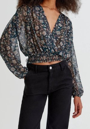Gennemsigtig sort bluse med blomsterprint, dyb v-hals, elastisk kant og lange pufærmer; parret med mørke sorte højtaljede bukser.
