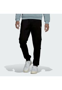 Pantalones cargo negros con bolsillos laterales, que presentan un corte relajado y puños en los tobillos, combinados con zapatillas blancas y un sudadera de color azul claro.