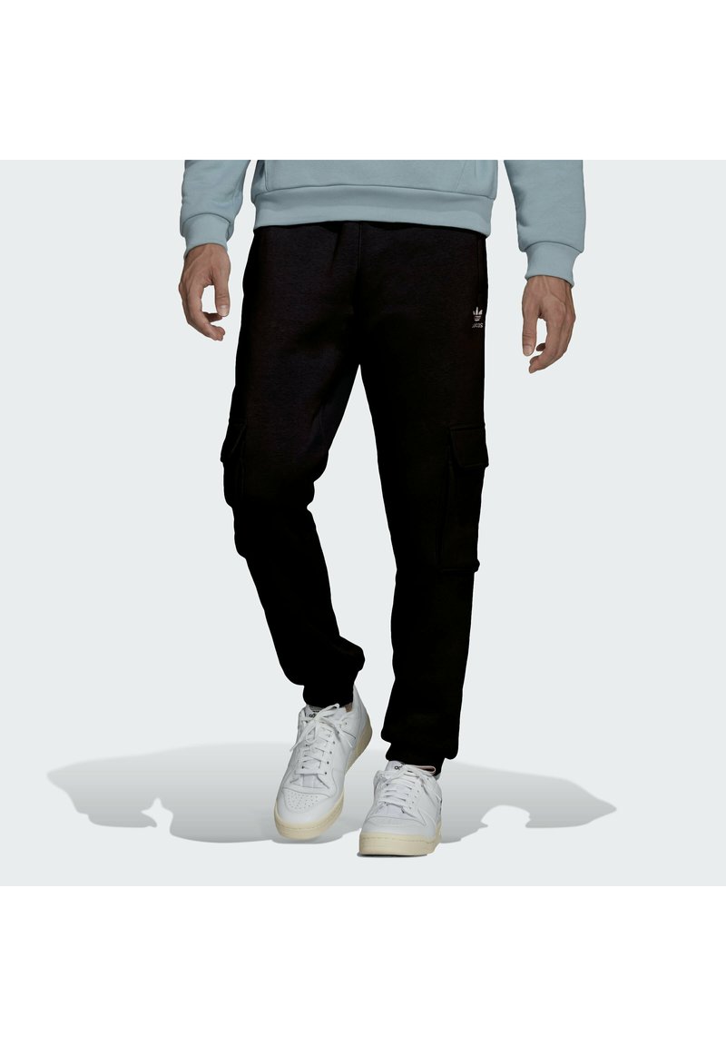 Pantalones cargo negros con bolsillos laterales, que presentan un corte relajado y puños en los tobillos, combinados con zapatillas blancas y un sudadera de color azul claro.