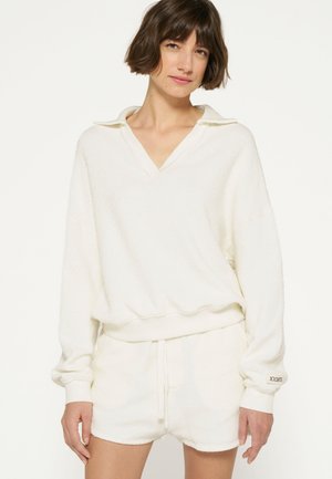 Felpa bianca e comoda con scollo a V, maniche lunghe e polsini a costine, abbinata a pantaloni corti bianchi coordinati. Tessuto morbido e texturizzato con un taglio rilassato.