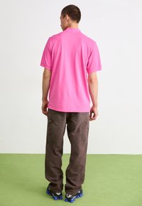 Rosa Kurzarm-Polohemd mit Kragen, kombiniert mit braunen Cargo-Hosen mit Taschen und grauen Sneakers mit blauen Sohlen.