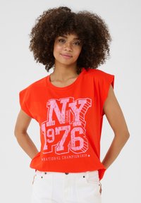 Raudona medvilninė T-shirt su trumpomis, nuleistomis rankovėmis. Dėvima balta grafika su užrašu "NY 1976" ir "NACIONALINĖ ČEMPIONATAS". Lygus paviršius.