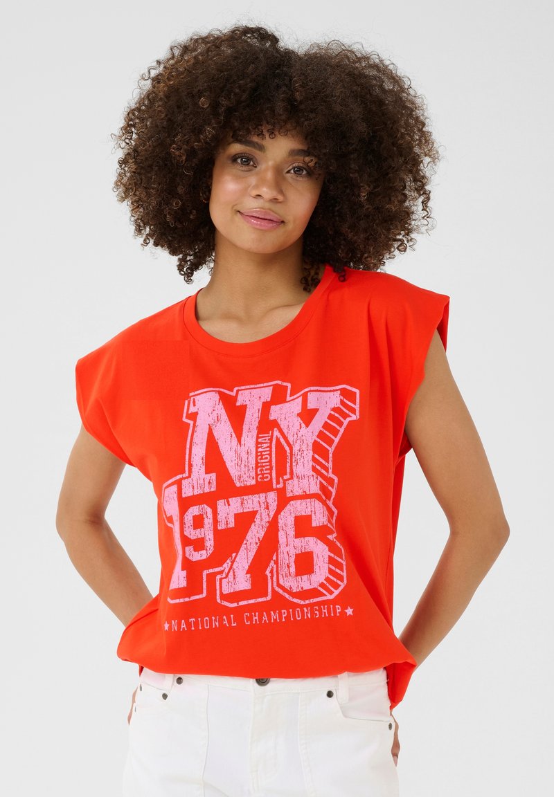 Raudona medvilninė T-shirt su trumpomis, nuleistomis rankovėmis. Dėvima balta grafika su užrašu "NY 1976" ir "NACIONALINĖ ČEMPIONATAS". Lygus paviršius.