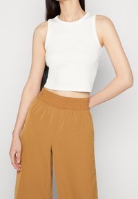 Hvid ærmeløs crop top i ribbet materiale, parret med højttaljede, brede lys brune bukser med elastisk talje og glat tekstur.