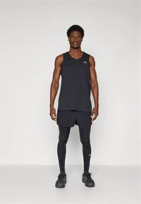 Černé sportovní tílko a kraťasy, doplněné těsnými černými legínami. Tílko má malé logo. Outfit dokončují texturované tenisky.