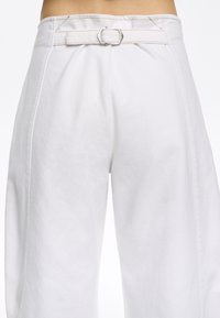 Witte wijde broek met een ceintuur met een zilveren gesp. De stof lijkt gestructureerd met zichtbare stikseldetails.