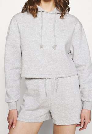 Personne portant un sweat à capuche court gris clair avec cordons et un short assorti taille haute avec ceinture à cordon.
