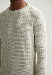 Gaiši pelēks adīts džemperis ar teksturētu, šūnu rakstu, ar apaļu kakla izgriezumu un garām piedurknēm, izgatavots no mīkstas auduma.