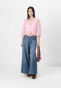 Crocheted pink cropped sweater, wide-leg blue denim jeans, brown shoulder bag, brown ankle boots. Textured patterns in the sweater.