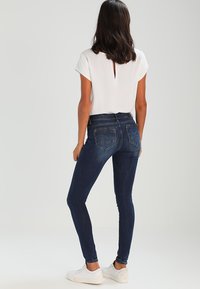 Μαύρη ψηλόμεση σκούρα μπλε εφαρμοστή τζιν παντελόνα με λεία υφή, που διαθέτει δύο πίσω τσέπες και εφαρμοστή γραμμή, συνδυασμένη με λευκή μπλούζα κοντομάνικη.