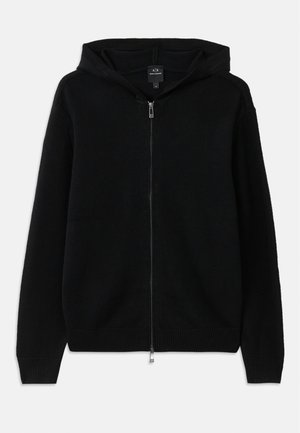 Svart hettegenser med glidelås laget av strikket stoff. Har hette, lange ermer og ribbede mansjetter og nederkant. Minimalistisk design uten mønstre.