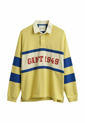 Gelbes Rugbyhemd mit langen Ärmeln, weißem Kragen, blauen horizontalen Streifen auf Ärmeln und Brust sowie rotem "GANT 1949"-Schriftzug auf der Brust.