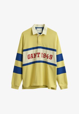 Gelbes Rugbyhemd mit langen Ärmeln, weißem Kragen, blauen horizontalen Streifen auf Ärmeln und Brust sowie rotem "GANT 1949"-Schriftzug auf der Brust.