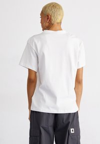 Camiseta blanca de algodón con un corte relajado, mangas cortas y cuello redondo, combinada con pantalones cargo grises con bolsillos laterales.
