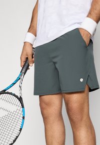 Ανδρικές αθλητικές βερμούδες σε σκούρο γκρι χρώμα, κατασκευασμένες από ένα λείο, ελαφρύ ύφασμα. Διαθέτουν ένα μικρό λογότυπο, πλαϊνές τσέπες και ελαφρώς πιο μακρύ πίσω στρίφωμα.