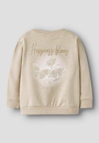 Sweatshirt beige avec des poignets et un ourlet côtelés ; le dos présente un texte métallisé "Le bonheur fleurit" et des illustrations de papillons blancs.