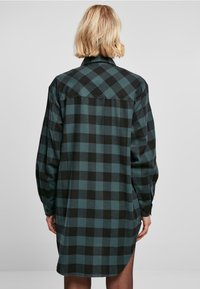 Rutete flanellskjorte i mørkegrønn og svart. Lange ermer, knappelukking ved håndleddene, bukket kant, og detaljer med ryggen med en avslappet passform.