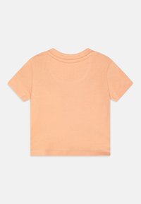 Camiseta de manga corta en algodón color durazno claro, con cuello redondo, textura suave y costuras remalladas.