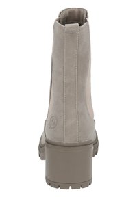 Botín de ante beige hasta el tobillo con un acabado texturizado, tacón grueso y suela de goma. Presenta un sutil branding en el tacón con un diseño aerodinámico.