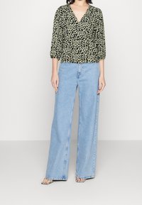 Grøn leopardprint bluse med V-hals, trekvartærmer, parret med lyseblå brede denimjeans og sort-hvide hælet sandaler.
