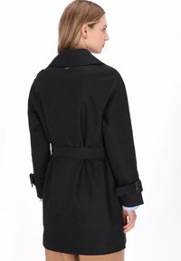 Palton negru cu talie cu curea, având un guler lat și manșete ajustabile. Textură netedă, design simplu și croială de lungime medie.