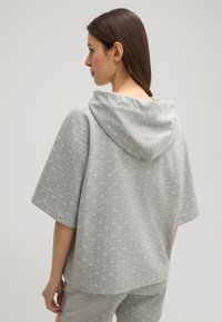 Grauer Kapuzenpulli aus weichem Stoff mit einem subtilen, sich wiederholenden Muster. Kurze Ärmel und lockere Passform, kombiniert mit passenden Shorts.