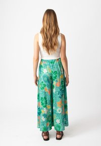 Bloemen, wijde broek met een groene basis, versierd met oranje, gele en blauwe bloemen. Elastische tailleband; lichtgewicht, vloeiende stof.