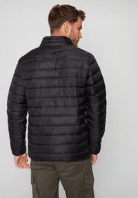 Chaqueta de plumas negra con textura acolchada horizontal, cuello alto y mangas largas. Material ligero, con un acabado suave.