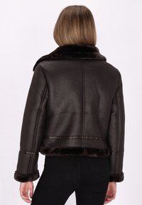 Donkerbruin leren jack met een cropped ontwerp, bontgevoerde kraag en manchetten, met een textuurfinish en naadloze stikdetails.
