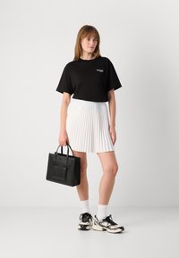 Svart kortermet T-skjorte med logo, hvit plisserte skjørt, svart veske, hvite sokker og svart/hvite joggesko. Enkle og kontrastfylte farger.