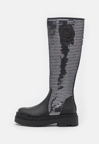 Botte noire montée jusqu'au genou avec une tige en maille texturée ornée de paillettes argentées. Semelle en caoutchouc noir solide avec un logo moulé sur le côté.