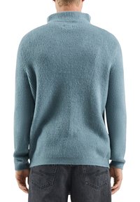 Jasnoniebieski, dziany sweter z wysokim kołnierzem, o fakturowanej powierzchni, długich rękawach i luźnym kroju, zestawiony z ciemnoszarymi dżinsami.