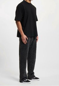 Svart oversized t-shirt med korta ärmar, kombinerad med texturerade svarta byxor med subtila mönster, iförd svarta sneakers.