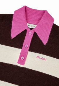 Ruskea ja kerma raidallinen neulepaita, jossa on vaaleanpunainen ribbikaulus ja kolme vaaleanpunaista nappia kauluksessa. Paidan etuosassa on vaaleanpunaisella brodeerattu teksti "Oh April".