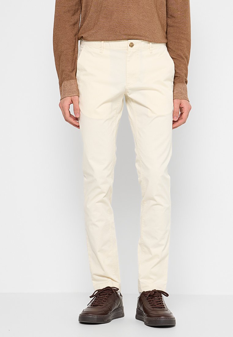 Chino couleur crème en coton, avec une coupe droite, des passants de ceinture et une fermeture à bouton à l'avant, associés à des baskets marron foncé.