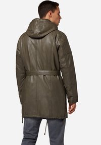 Olivgrön läderjacka med huva, vadderade axlar, midjebälte och dragsko nederkant. Texturerad yta och sidogylfter synliga.