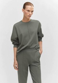 Olijfgroene sweater en bijpassende broek van een zachte, gestructureerde stof. De top heeft een ronde halslijn en licht gepofte mouwen.