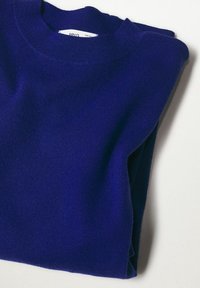 Pull col rond bleu marine uni plié en tissu tricoté doux sur une surface blanche et plate.
