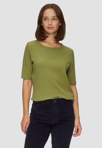 Oliwkowa, prążkowana bluzka z krótkim rękawem i okrągłym dekoltem, połączona z ciemnogranatowymi spodniami z cordurowego materiału z bocznymi kieszeniami.