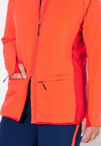 Czerwona i pomarańczowa ocieplana kurtka z przednim zamkiem błyskawicznym, bocznymi kieszeniami i kontrastowym materiałem na rękawach. Gładka faktura z detalami szwów.