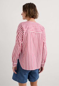 Camicia a maniche lunghe a righe rosse e bianche con spallina posteriore, polsini con bottone e vestibilità comoda, abbinata a pantaloni corti di denim.