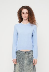 Ανοιχτό μπλε πλεκτό πουλόβερ με μακριά μανίκια και υφασμένο λευκό βολάν γιακά, συνδυασμένο με γκρι φούστα με σχέδιο φίδι.