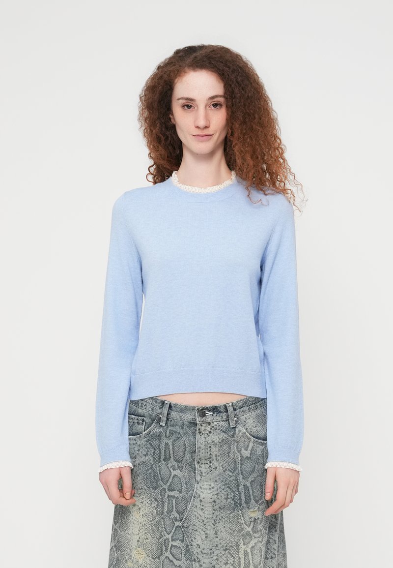 Ανοιχτό μπλε πλεκτό πουλόβερ με μακριά μανίκια και υφασμένο λευκό βολάν γιακά, συνδυασμένο με γκρι φούστα με σχέδιο φίδι.