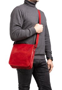 Borsa a tracolla in pelle rossa con una texture liscia e raffinata, tracolla regolabile e forma rettangolare, indossata a tracolla.