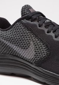 Sneaker nera con tomaia in mesh testurizzato, con logo Nike grigio e lacci neri. La suola è slanciata e leggermente rialzata.