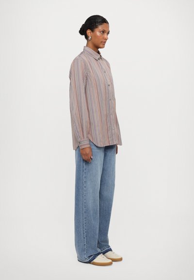 Gestreifte Button-down-Bluse in Pastellfarben, kombiniert mit weit geschnittenen, hellblauen Jeans und beigen Schuhen, was einen lässigen, entspannten Look schafft.
