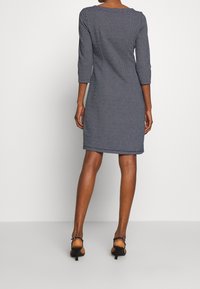 Marinblå klänning med trekvartslånga ärmar, texturerad tyg och en figurnära silhuett. Förstärkt med ett subtilt mönster. Bärs med svarta klacksandaler.