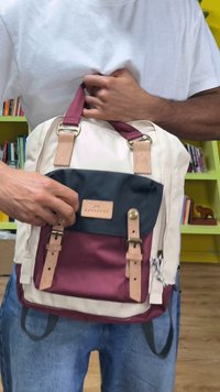 Rygsækken har cremefarvet stof, bordeaux detaljer, mørkeblå klap, læderstropper og en frontlomme med trykknapslukning og spænder.