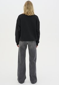 Černá oversized mikina s spadlými rameny, v kombinaci s šedými džíny s vysokým pasem a širokými nohavicemi. Hladká textura, pohodlný design.